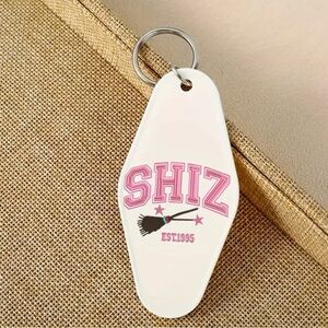 Wicked Themed Motel Keychain That is White and says “SHIZ” in Pink NEW